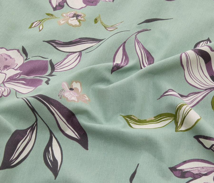 Zbliżenie miętowej tkaniny w kwiaty w odcieniach fioletu, bieli i zieleni.