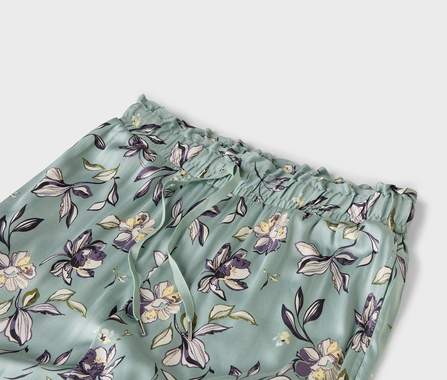 Zbliżenie na jasnoniebieskie spodnie we wzory kwiatowe, z elastycznym pasem i sznurkiem.