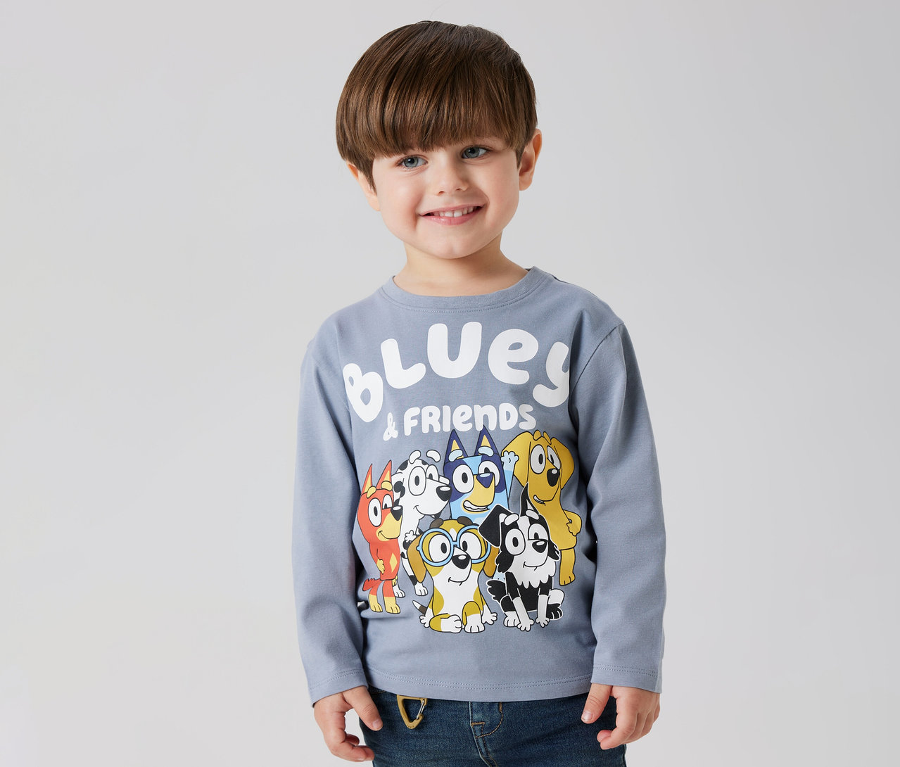 Uśmiechnięty chłopiec ma na sobie koszulkę z długim rękawem NAME IT „BLUEY” z motywem Bluey i przyjaciół.