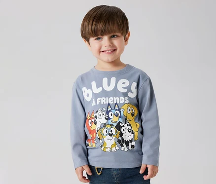 Uśmiechnięty chłopiec ma na sobie koszulkę z długim rękawem NAME IT „BLUEY” z motywem Bluey i przyjaciół.
