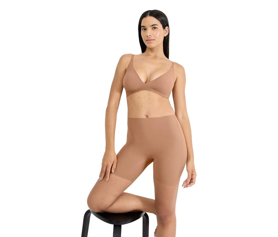 Kobieta pozuje na stołku, ma na sobie biustonosz i modelujące szorty w cielistym kolorze.