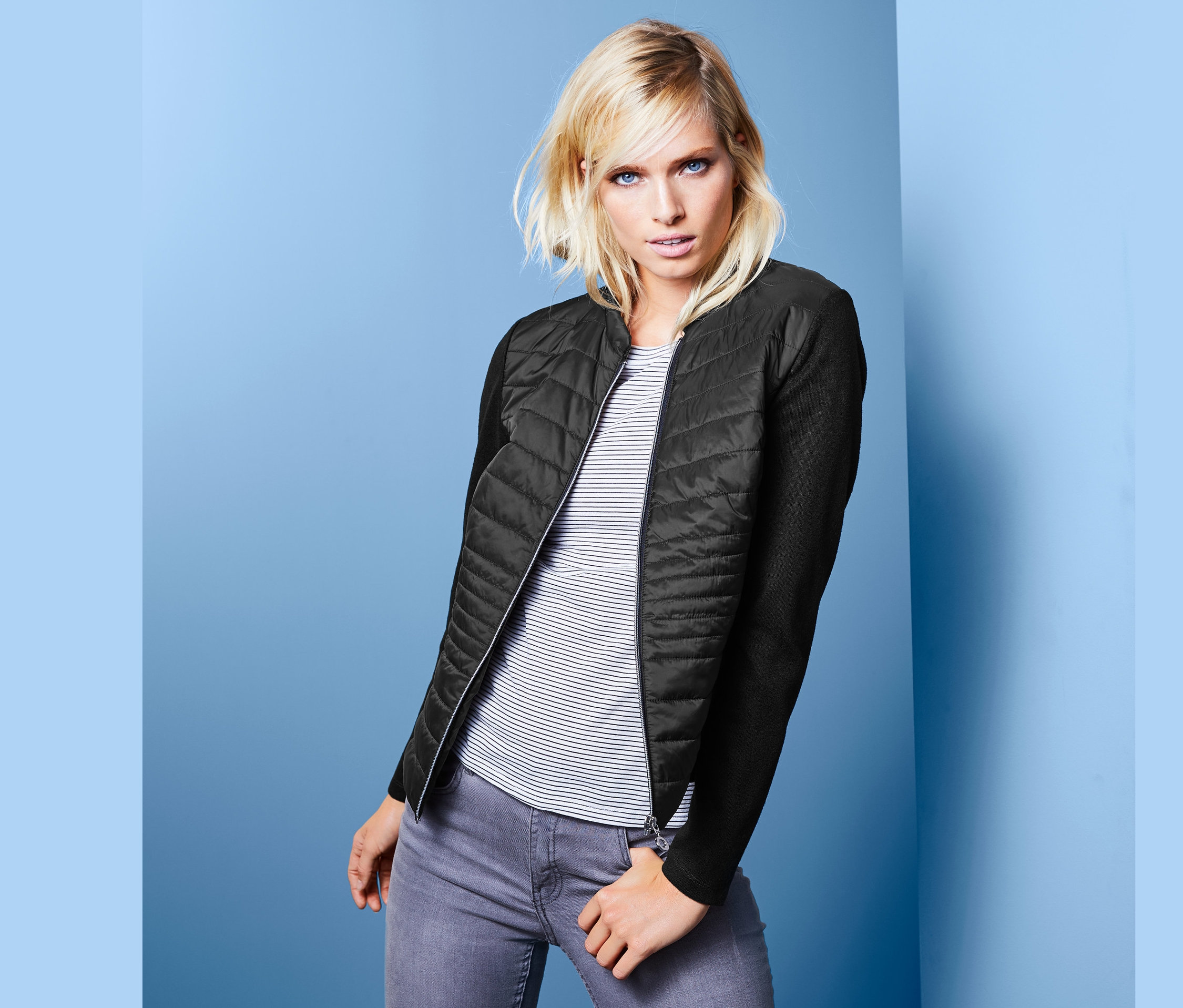 Blondwłosa kobieta pozuje w damskiej pikowanej kurtce z materiałowymi rękawami.