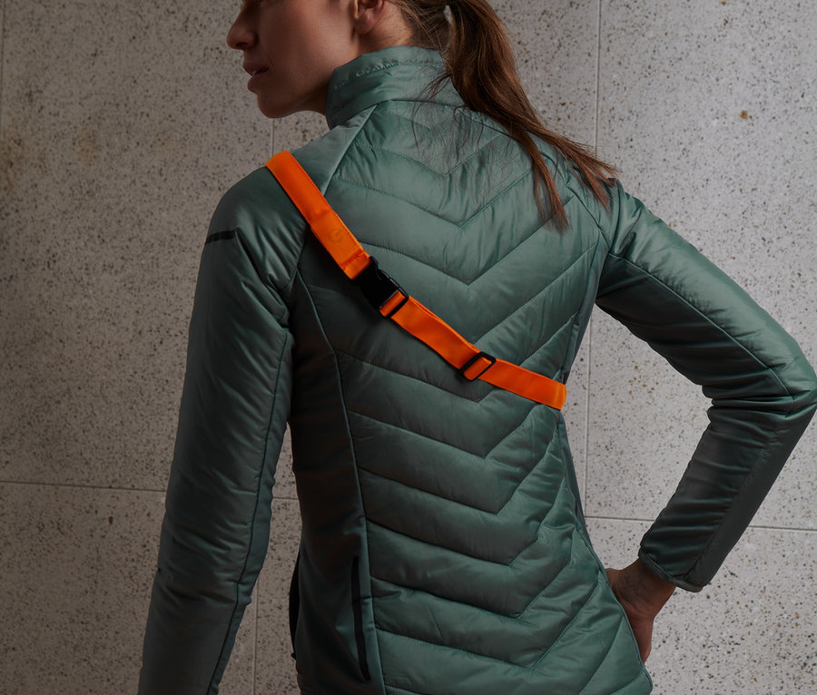 Kobieta ma na sobie zieloną kurtkę i pomarańczowy pasek LED.