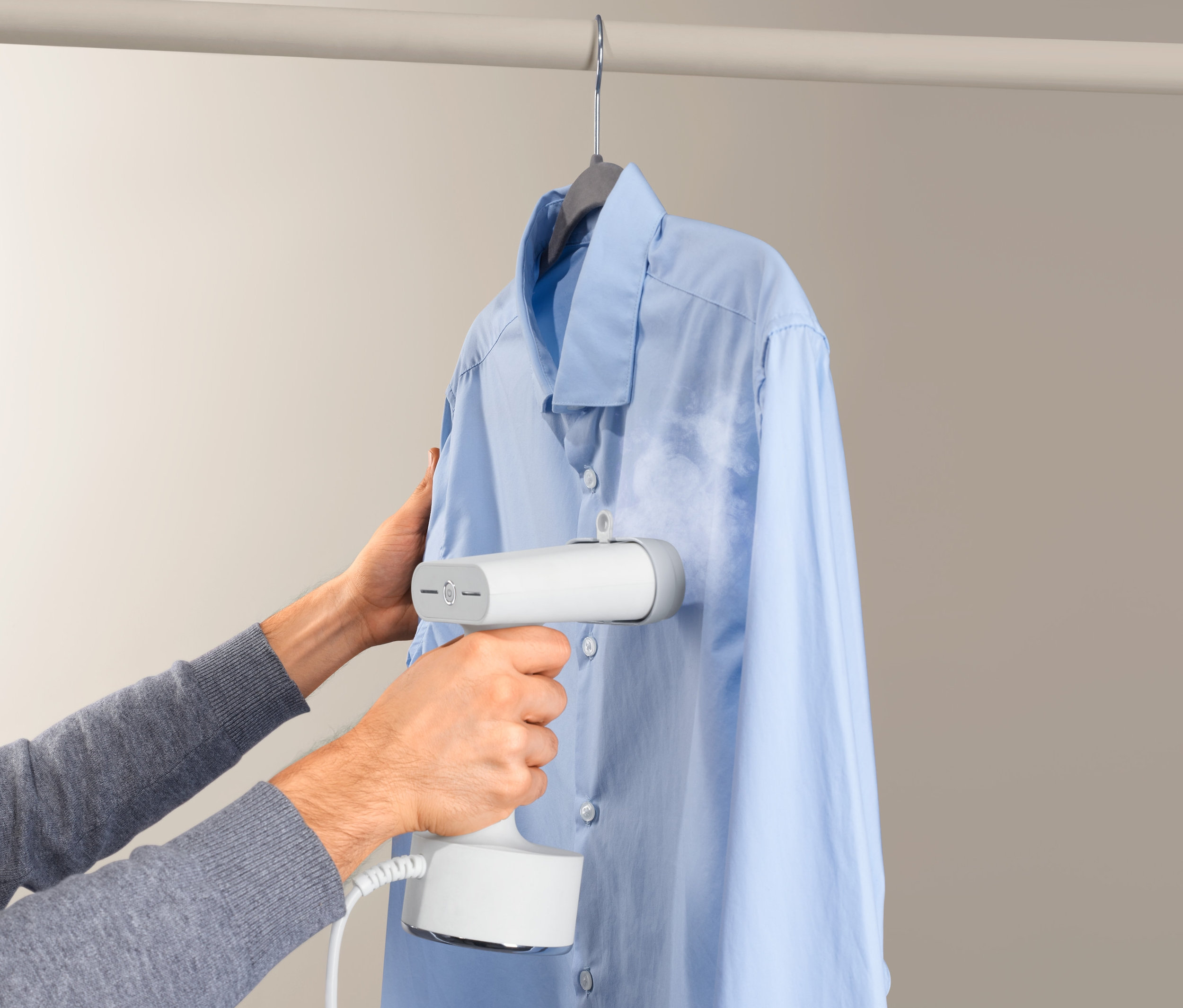 Mężczyzna używa parownicy do ubrań na jasnoniebieskiej koszuli wiszącej na wieszaku.