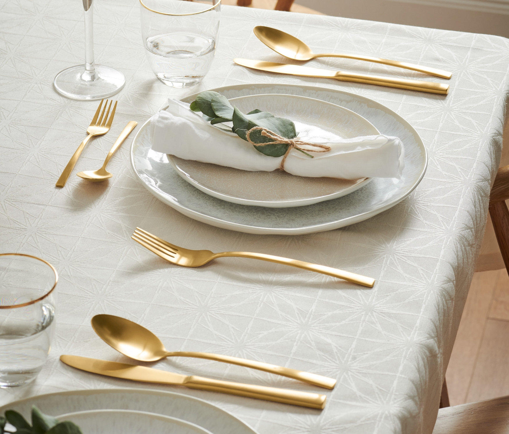 Nakryty stół z talerzami, szklankami i złotym zestawem sztućców.