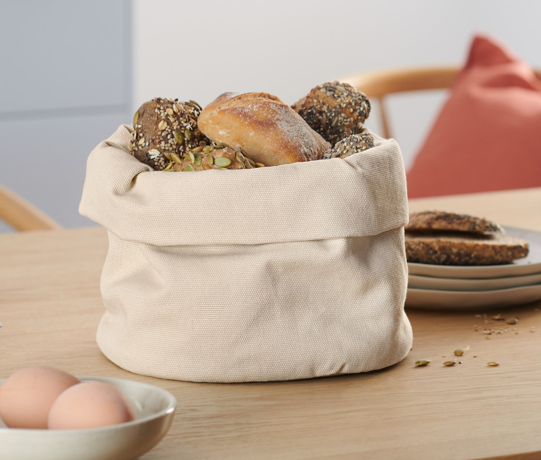 Na stole stoi beżowy koszyk na pieczywo wypełniony wypiekami.