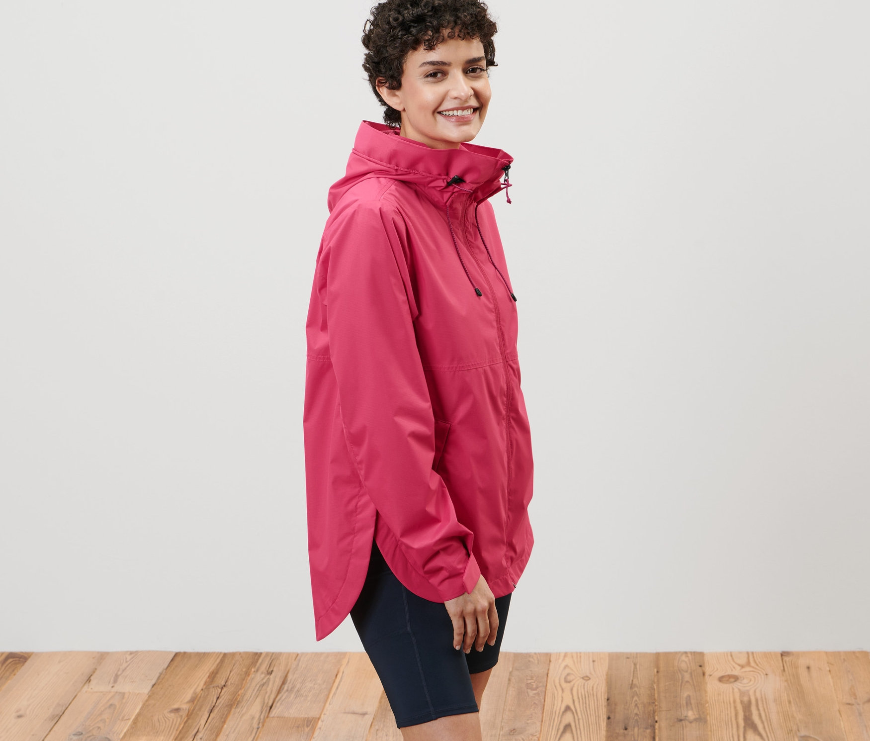 Kobieta pozuje w różowej kurtce przeciwdeszczowej.