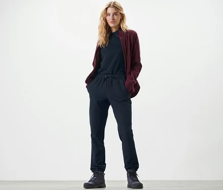 Blondwłosa kobieta stoi z rękami w kieszeniach spodni dresowych softshell.