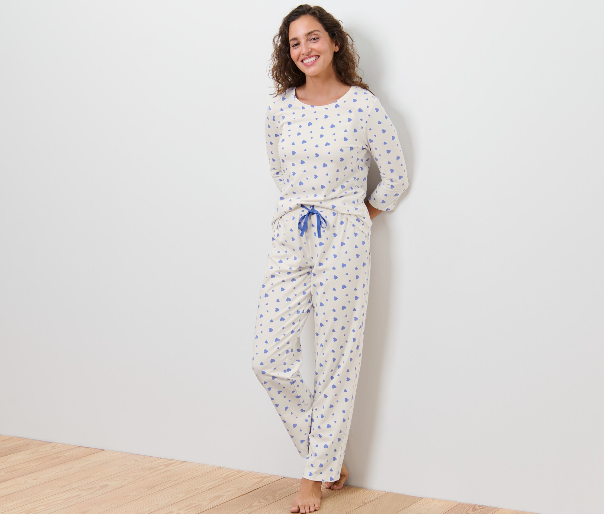 Kobieta opiera się o ścianę, ubrana w piżamę w serduszka.