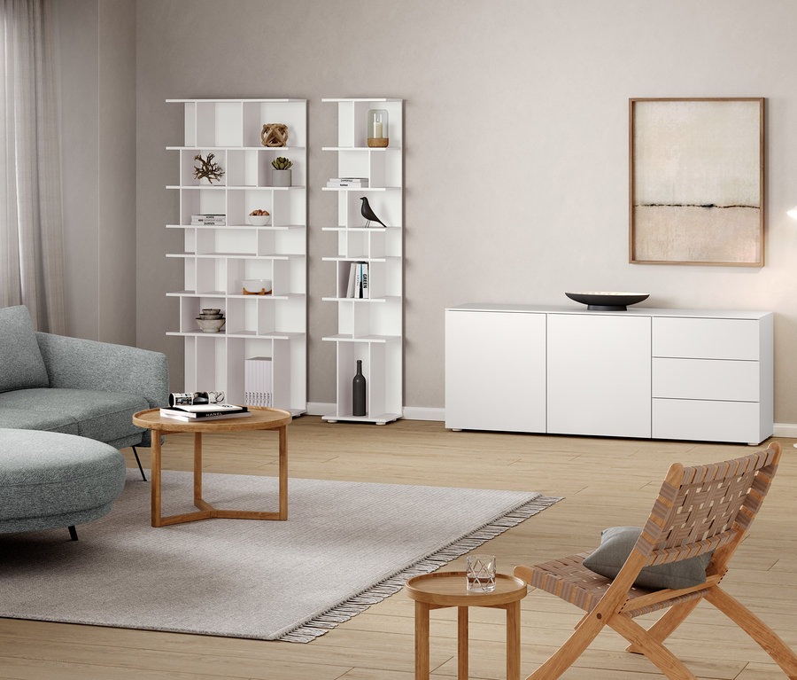 Pokój dzienny z szarą sofą, okrągłym stolikiem, szafką typu sideboard, regałem o szerokości ok. 80 cm i białą metalową lampą podłogową »Cale«.