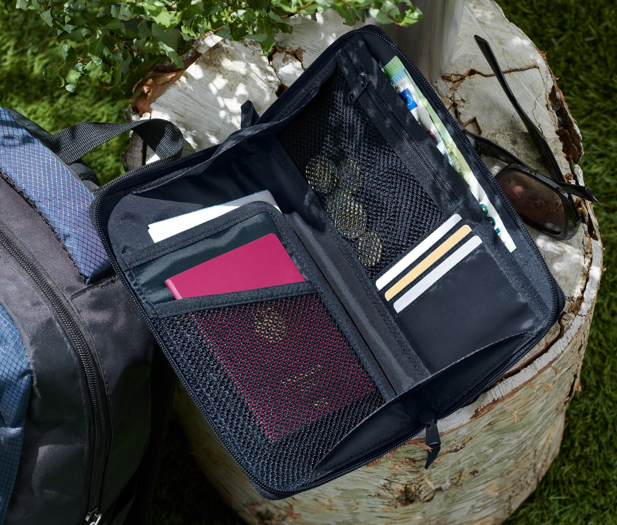 Otwarta, czarna teczka na dokumenty leży na pniu drzewa obok niebiesko-czarnego plecaka.