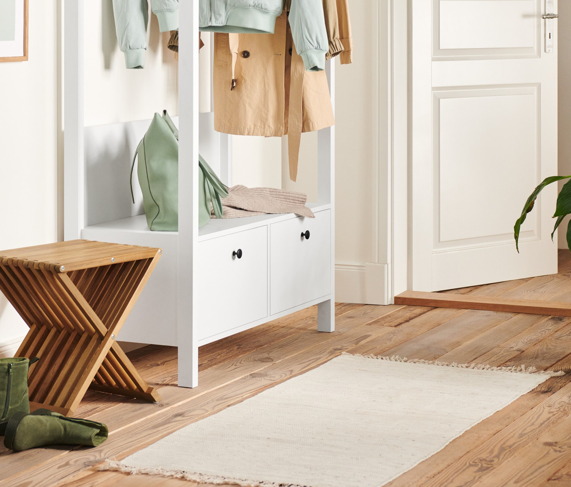 W przedpokoju stoi biała garderoba z dużymi szufladami i składany hocker. Na garderobie leżą zielona torebka i sweter.