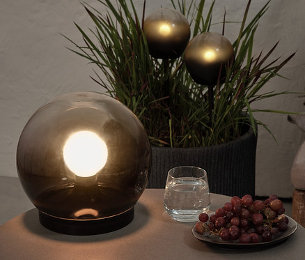Na stole stoi kula świetlna z dymionego szkła, szklanka wody i winogrona. W tle, w doniczce, znajdują się 2 kule świetlne LED.