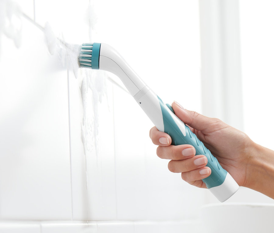 Ręka trzyma elektryczną szczotkę czyszczącą i czyści nią białe płytki.