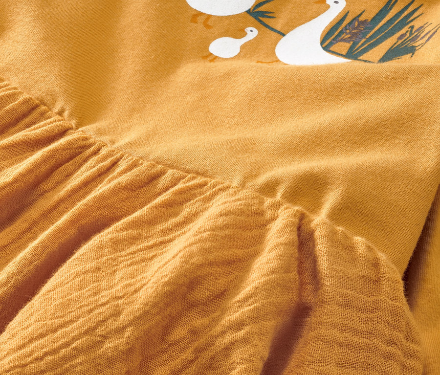 Zbliżenie na żółtą sukienkę niemowlęcą z tkaniny z nadrukiem gęsi.