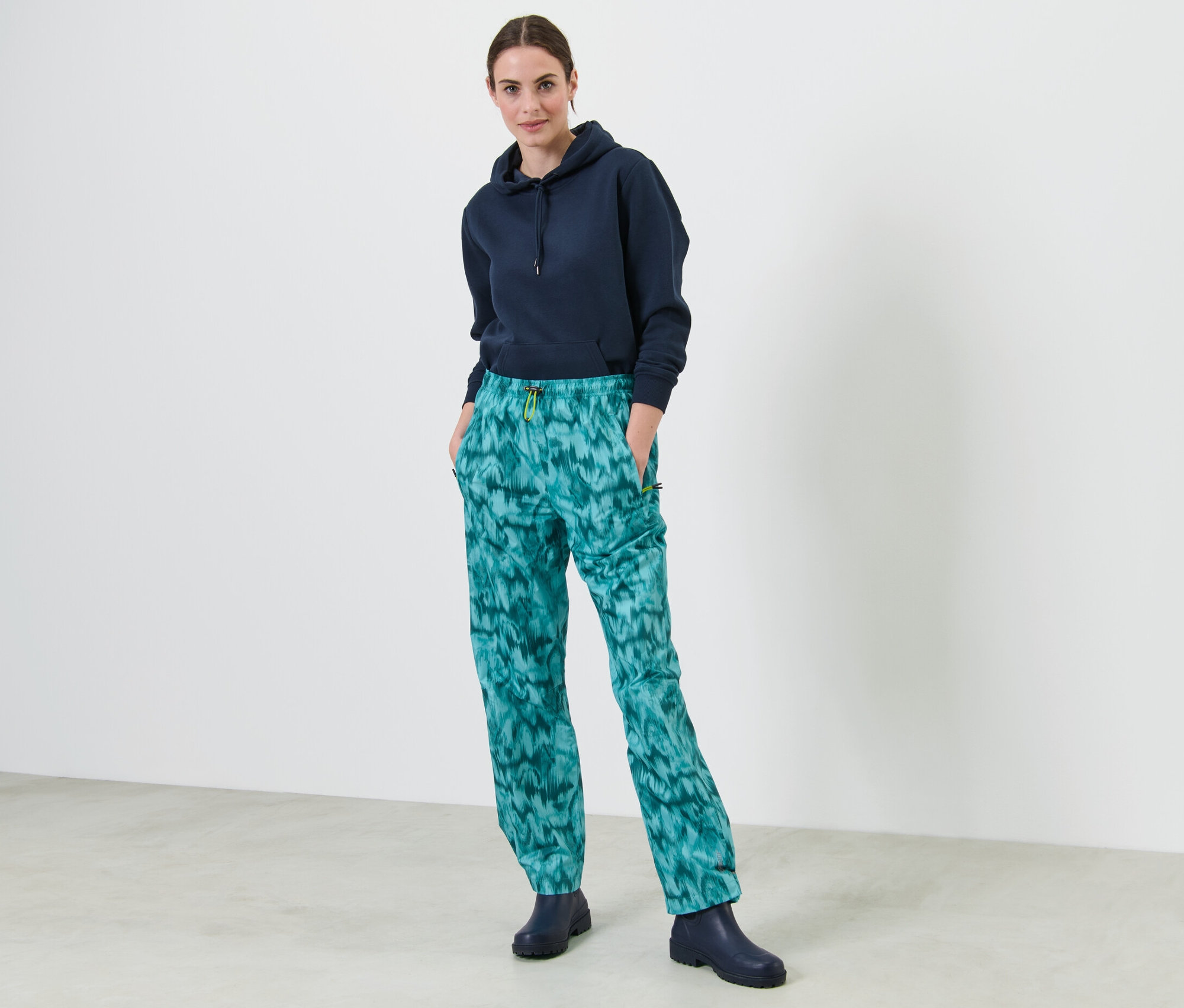 Kobieta stoi z rękami w kieszeniach spodni przeciwdeszczowych z nadrukiem.