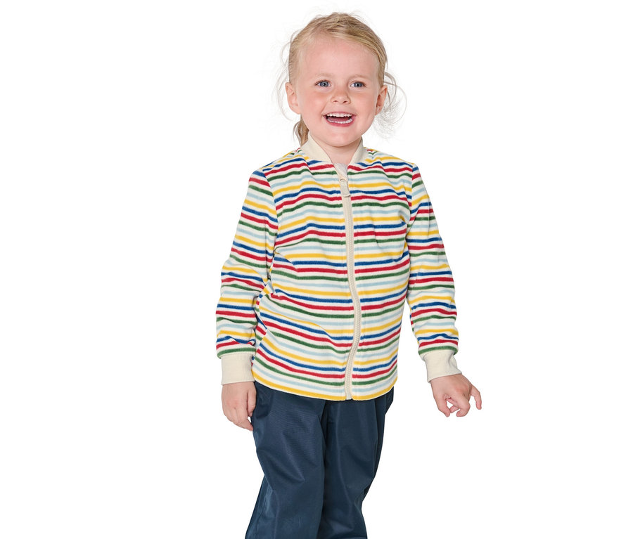 Uśmiechnięta blondynka ma na sobie kurtkę w paski i niebieskie spodnie.
