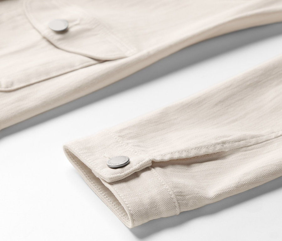 Zbliżenie na jasno-beżową kurtkę dżinsową z kieszeniami cargo, ukazujące kieszeń na piersi i mankiet rękawa.