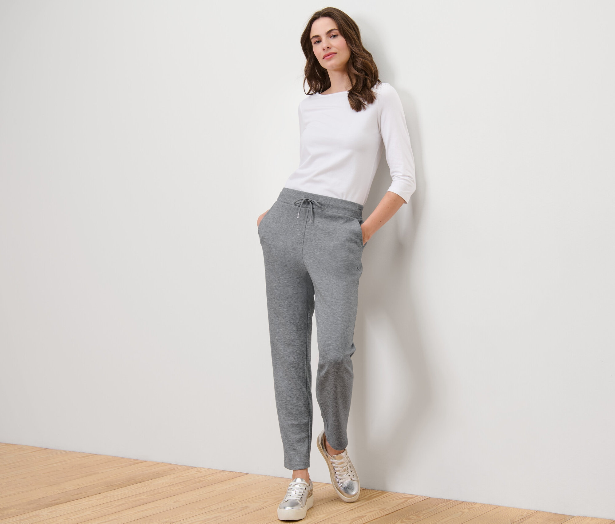 Kobieta pozuje w szarych spodniach dresowych i białym topie.