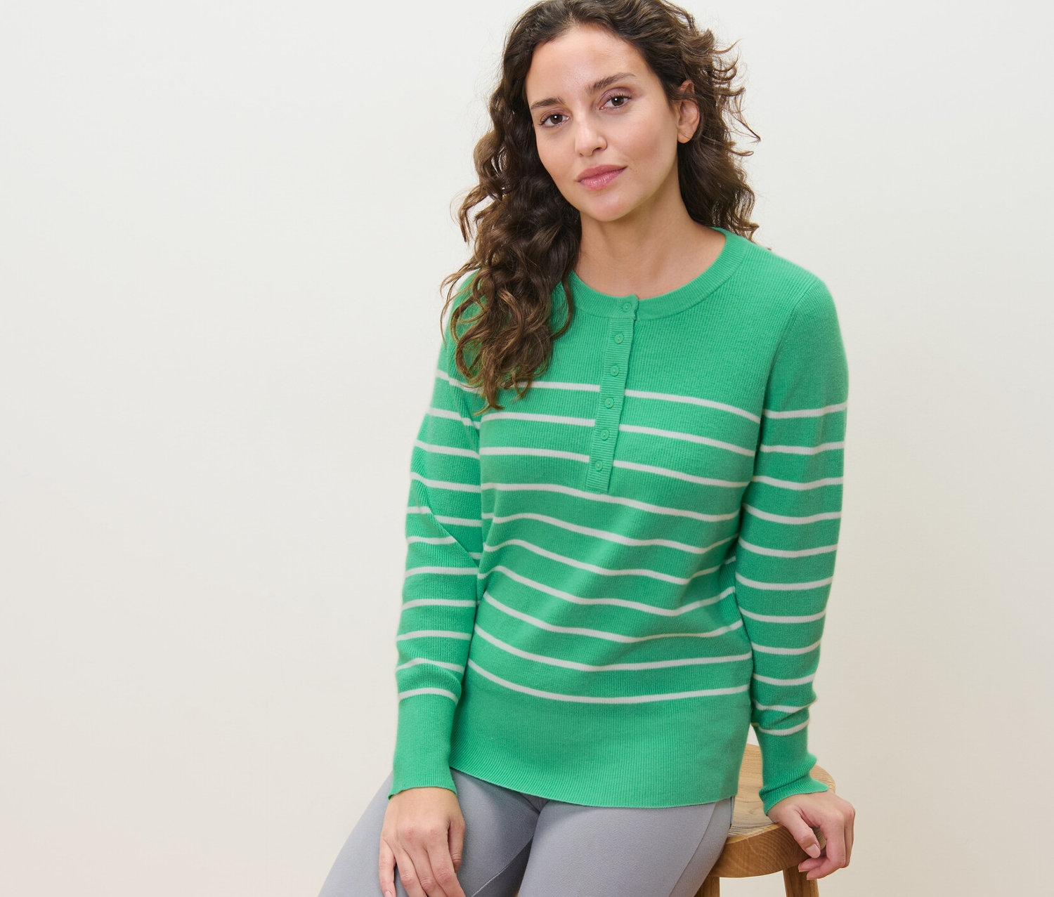 Kobieta siedzi na stołku i ma na sobie zielony sweter w paski.