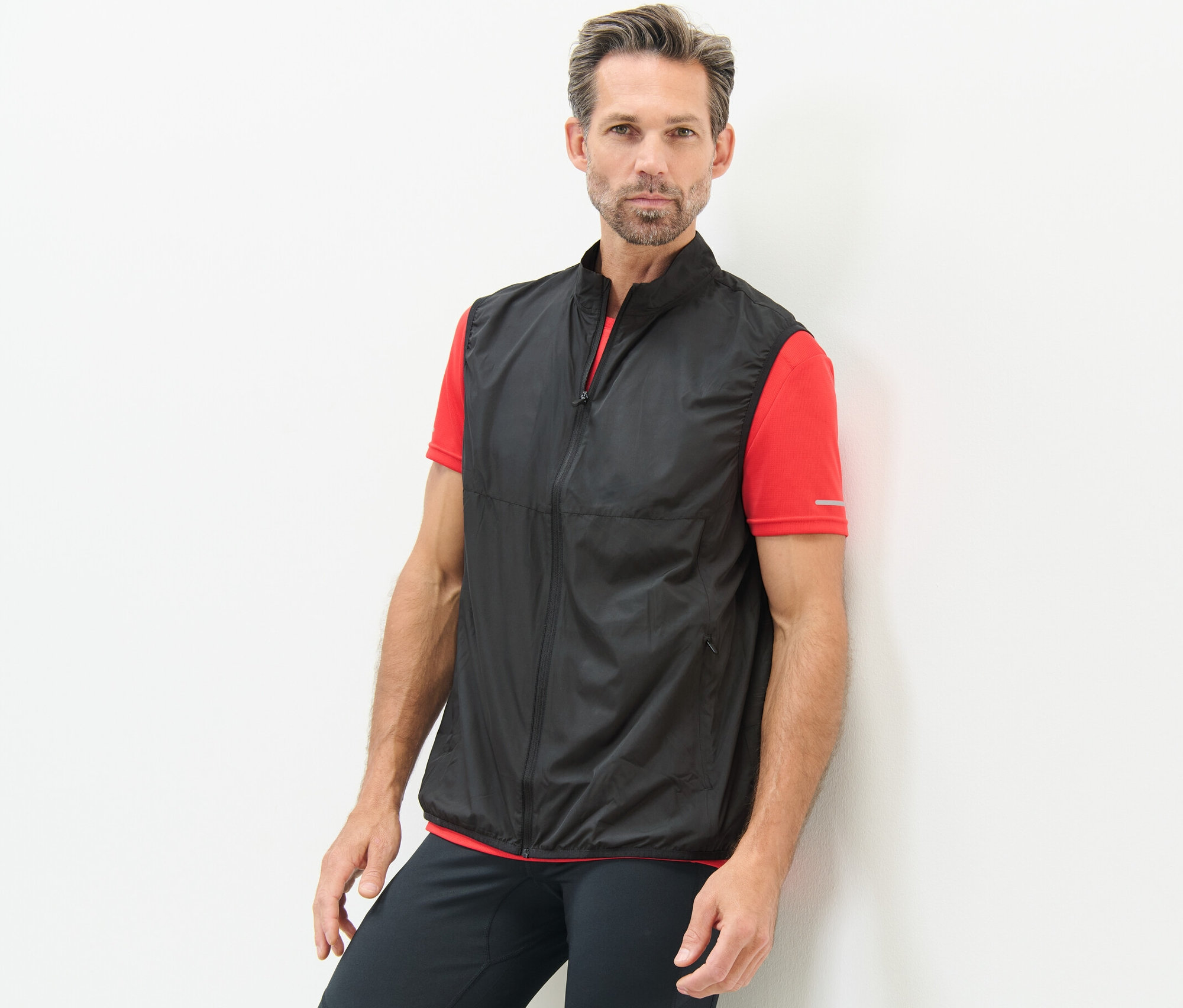 Mężczyzna oparty o ścianę w kamizelce funkcyjnej.