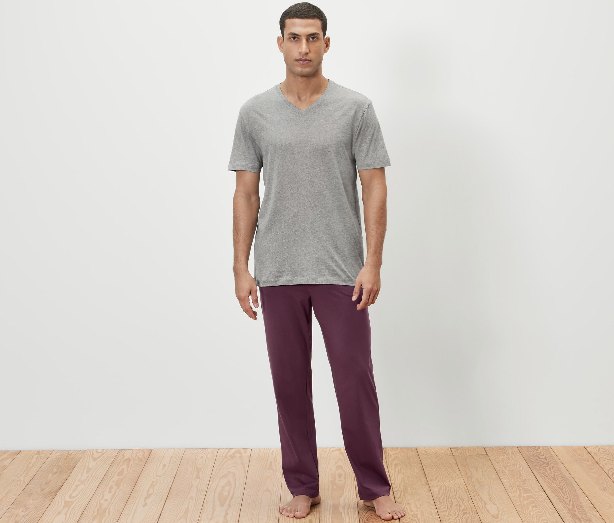Mężczyzna ma na sobie szary t-shirt i bordowe spodnie od piżamy.
