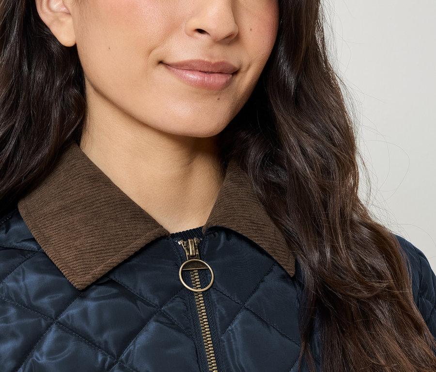 Zbliżenie na damską kurtkę pikowaną z brązowym kołnierzem sztruksowym i złotym zamkiem błyskawicznym.