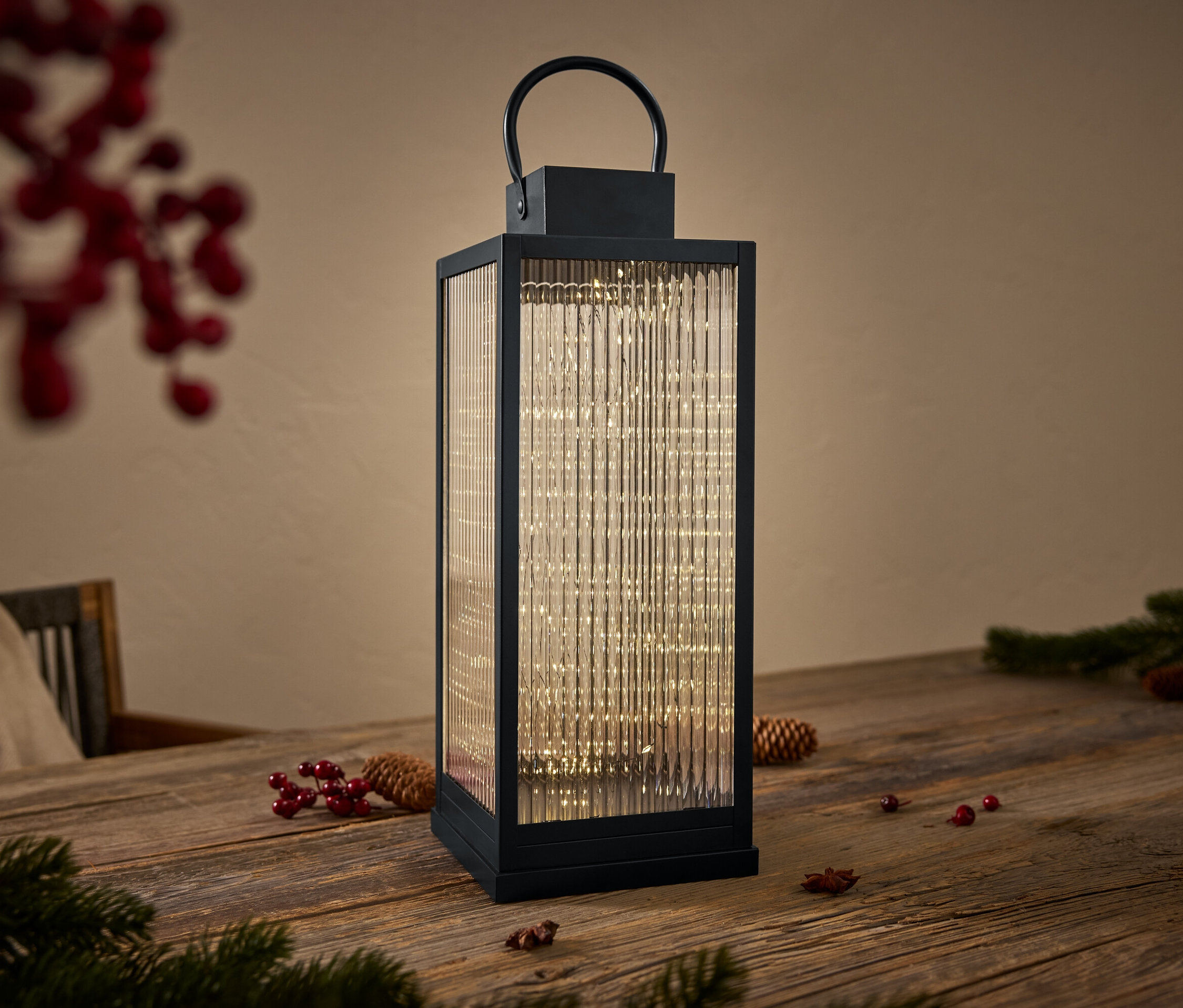 Czarny lampion ze szklanymi ścianami i światełkami w środku stoi na drewnianym stole.