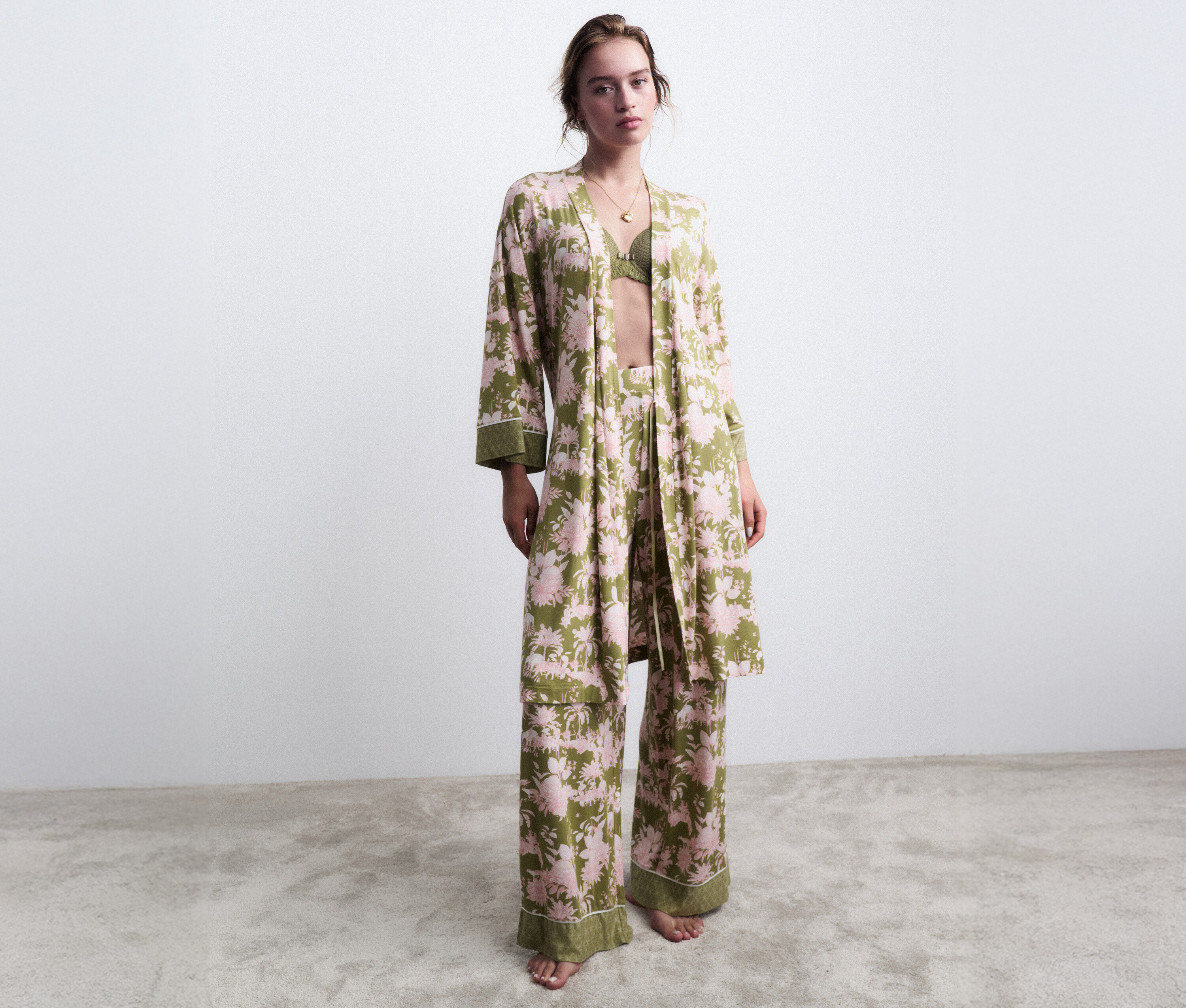 Kobieta stoi boso w zielonej piżamie w kwiaty z pasującym szlafrokiem.