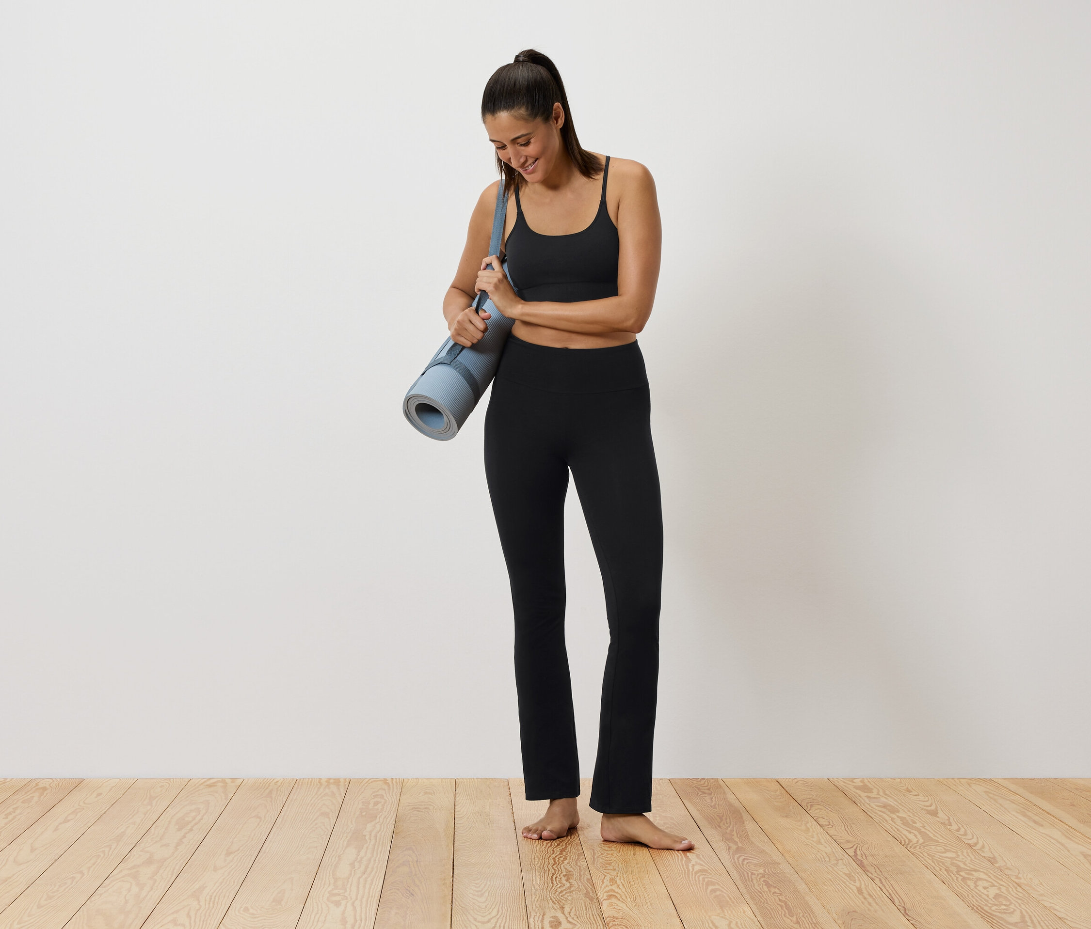 Kobieta w czarnym stroju sportowym trzyma matę do jogi.