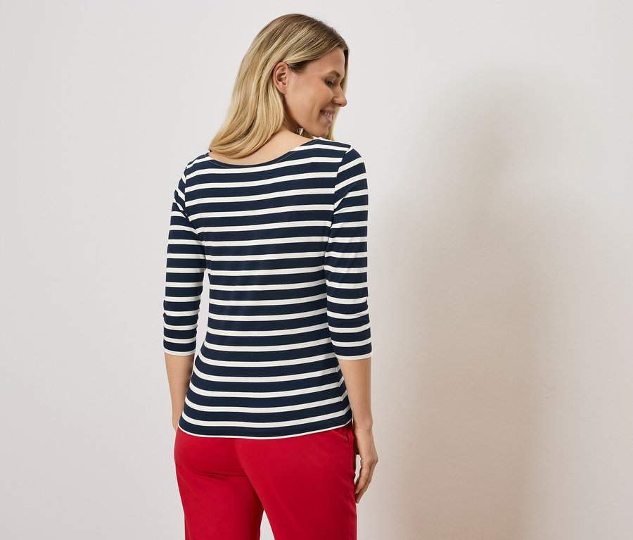 Blondynka w bluzce w paski granatowo-białe i czerwonych spodniach.