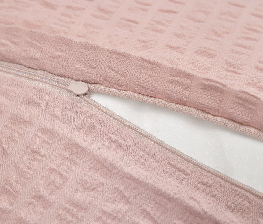 Szczegół różowej pościeli z teksturą i zamkiem błyskawicznym, częściowo odsłaniającym białe wnętrze.