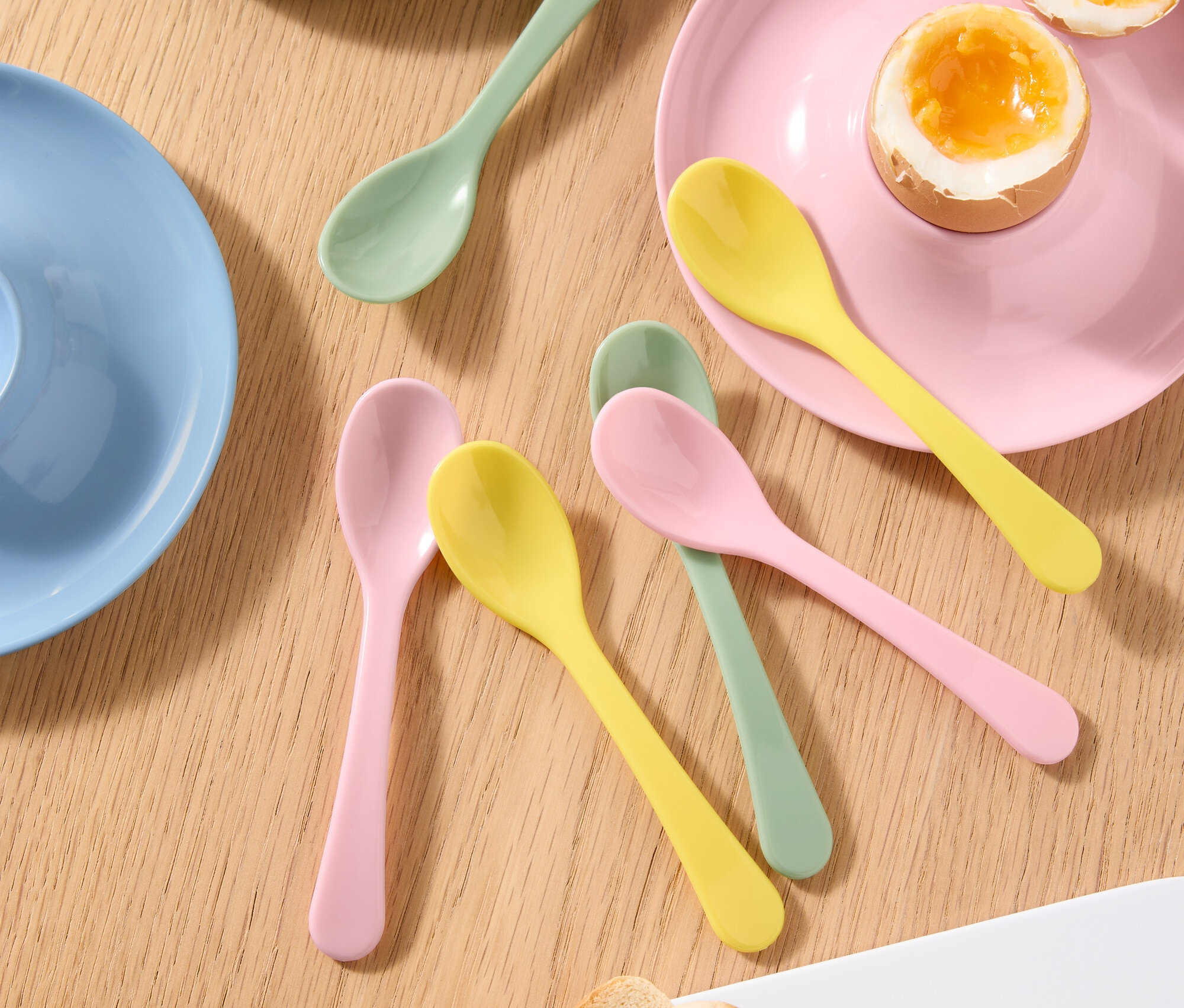 Widok z góry na stół z jajkiem na miękko w kieliszku do jajek, przekrojonym na pół jajkiem na miękko na talerzu, kolorowymi łyżkami i tostami.