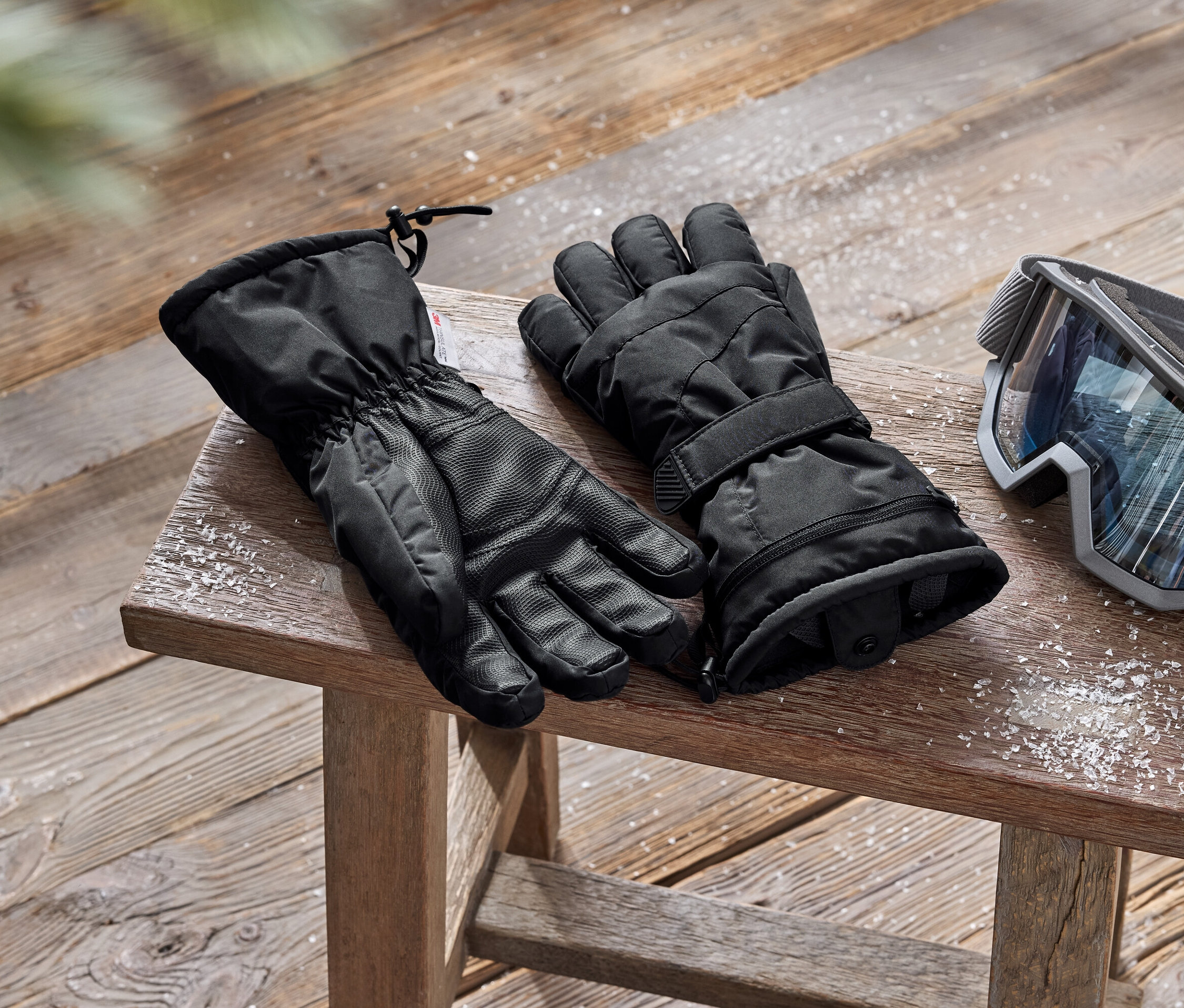 Czarne rękawice narciarskie i gogle leżą na drewnianym stołku.