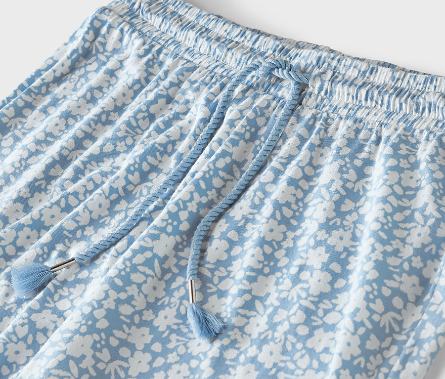Szczegół jasnoniebieskich spodni z białym kwiatowym wzorem, elastycznym pasem i niebieskim sznurkiem.
