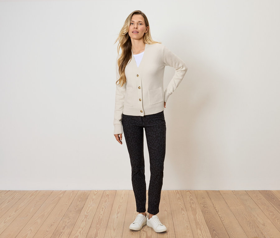 Blondynka pozuje w kremowym kardiganie, czarnych wzorzystych spodniach i białych tenisówkach.