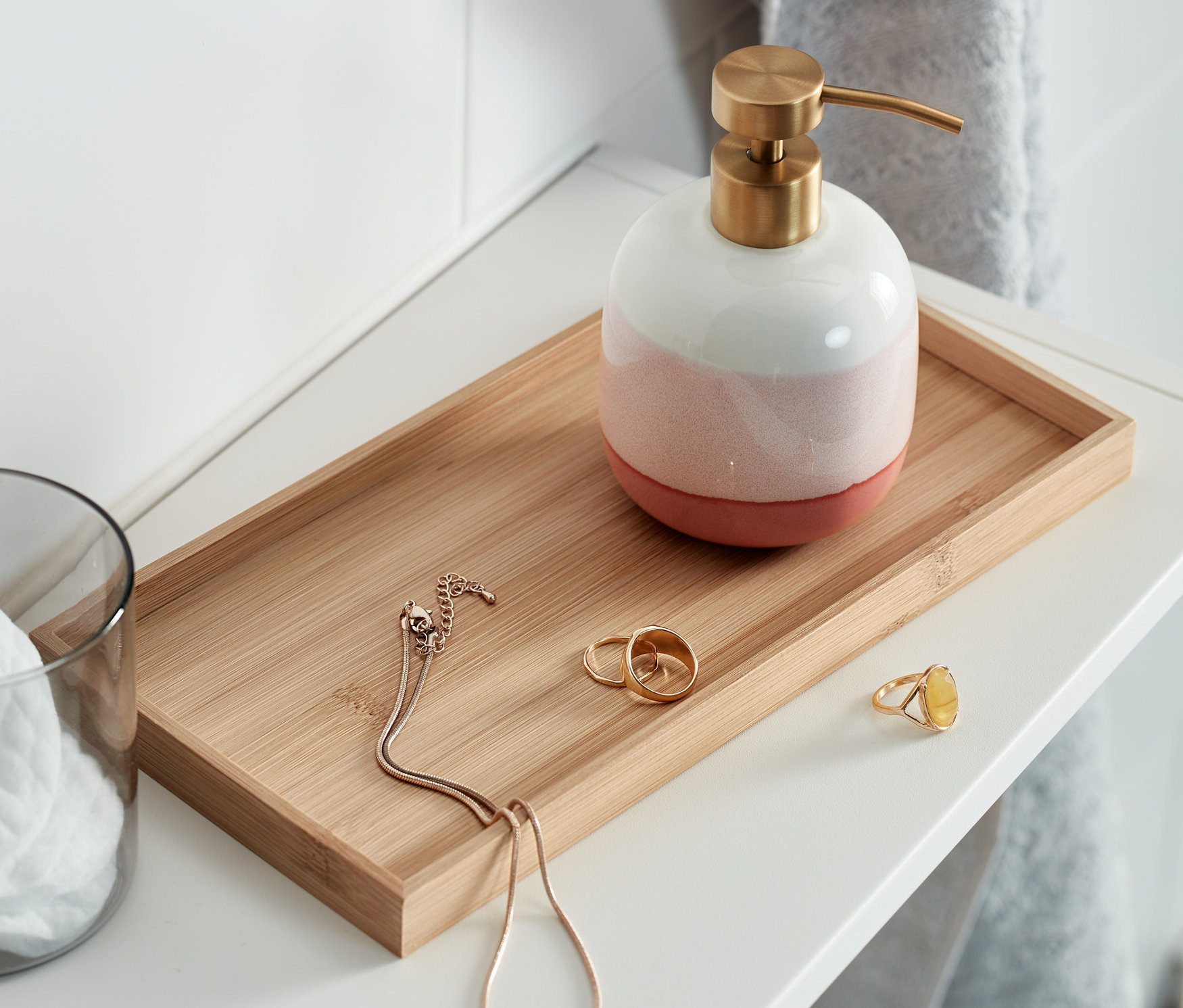 Na białej półce znajduje się dekoracyjna taca z dozownikiem do mydła, szklanką z wacikami i biżuterią.