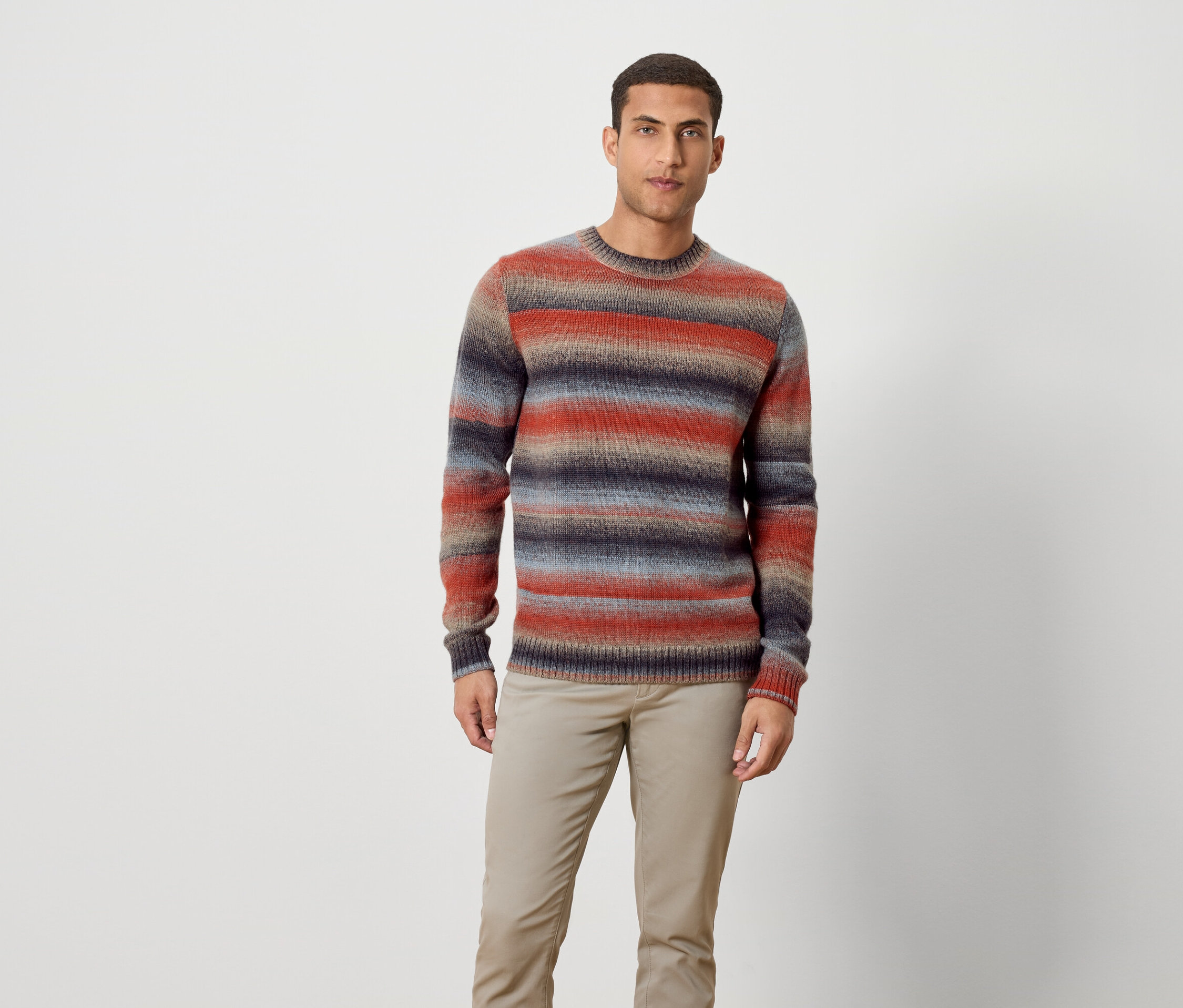 Mężczyzna stoi w pasiastym swetrze i spodniach.