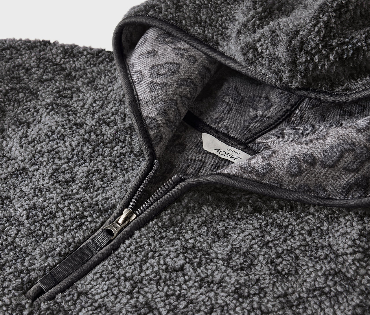 Zbliżenie szarej, kudłatej bluzy z kapturem zapinanej na zamek błyskawiczny i szarym zwierzęcym wzorem po wewnętrznej stronie kaptura.