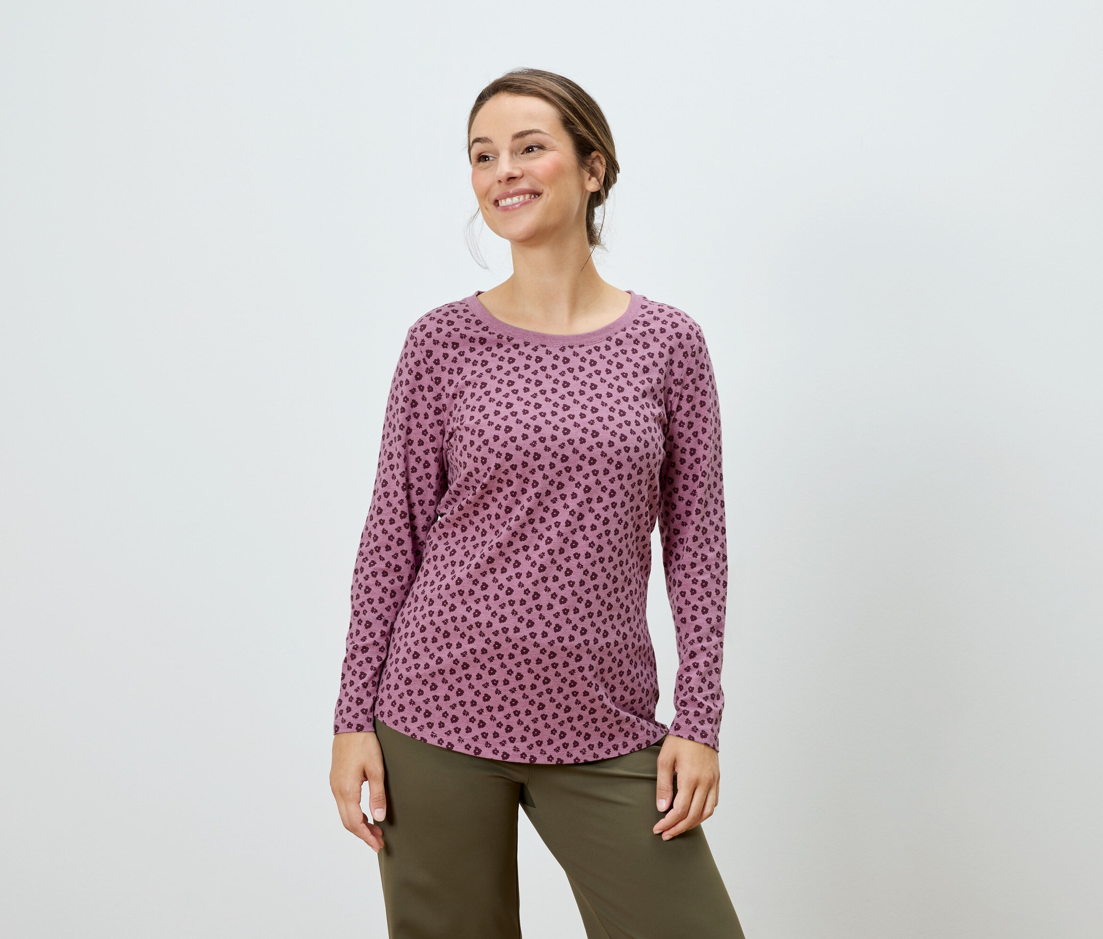 Kobieta pozuje w różowej bluzce z długim rękawem w kropki i zielonych spodniach.