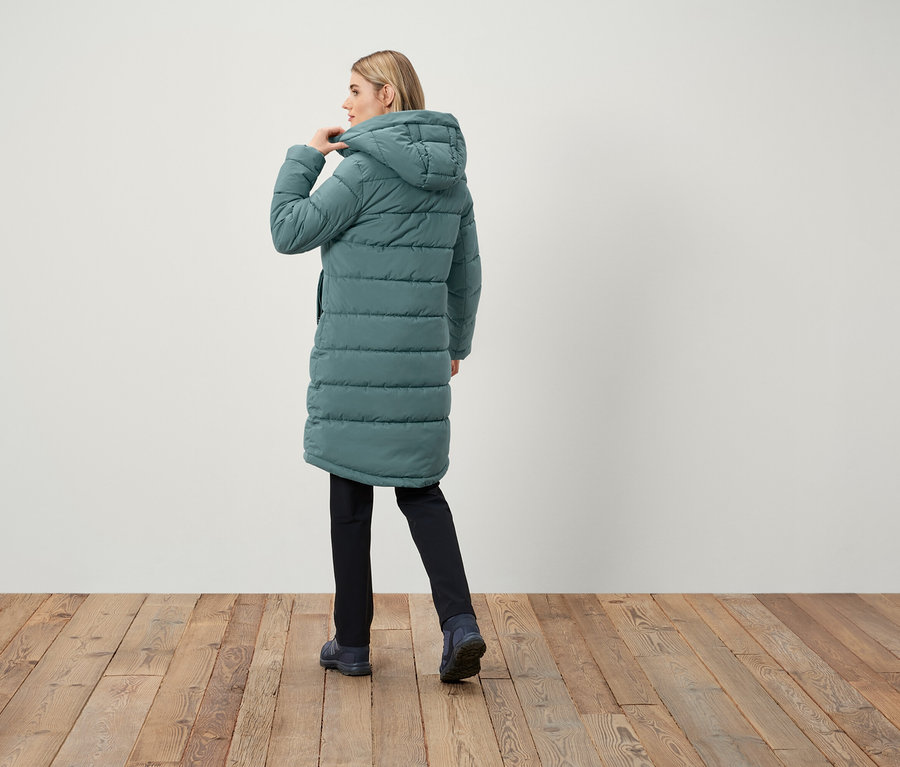 Kobieta w długim, pikowanym płaszczu z kapturem, tyłem do kamery.