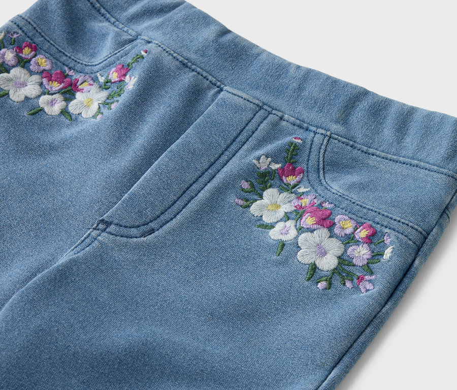 Zbliżenie jasnoniebieskich dżinsów z haftowanymi kwiatami na pasie i kieszeni.