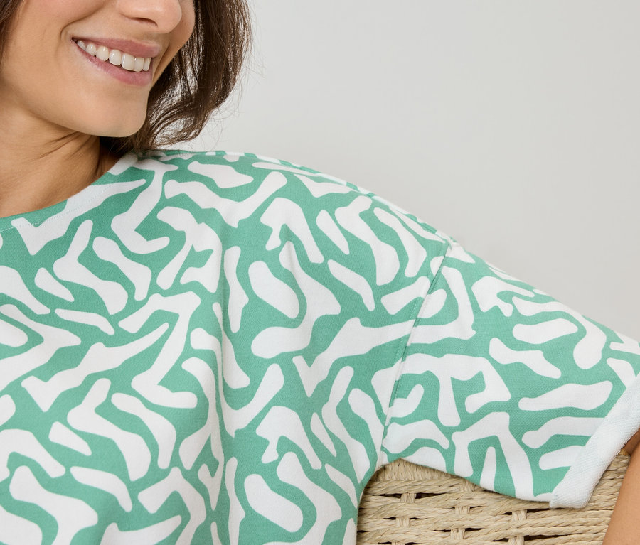 Kobieta ma na sobie bluzkę w zielono-biały wzór.