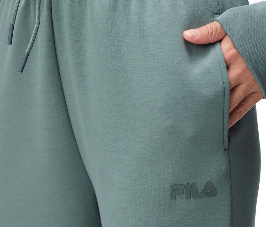 Zbliżenie na osobę w zielonych spodniach do biegania Fila ze ściągaczem i sznurkiem w pasie oraz ręką w kieszeni.