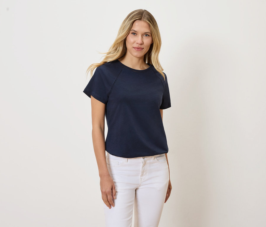 Blondwłosa kobieta ma na sobie granatowy T-shirt i białe dżinsy.