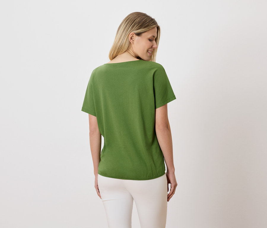 Kobieta o blond włosach ma na sobie zielony T-shirt i białe spodnie.