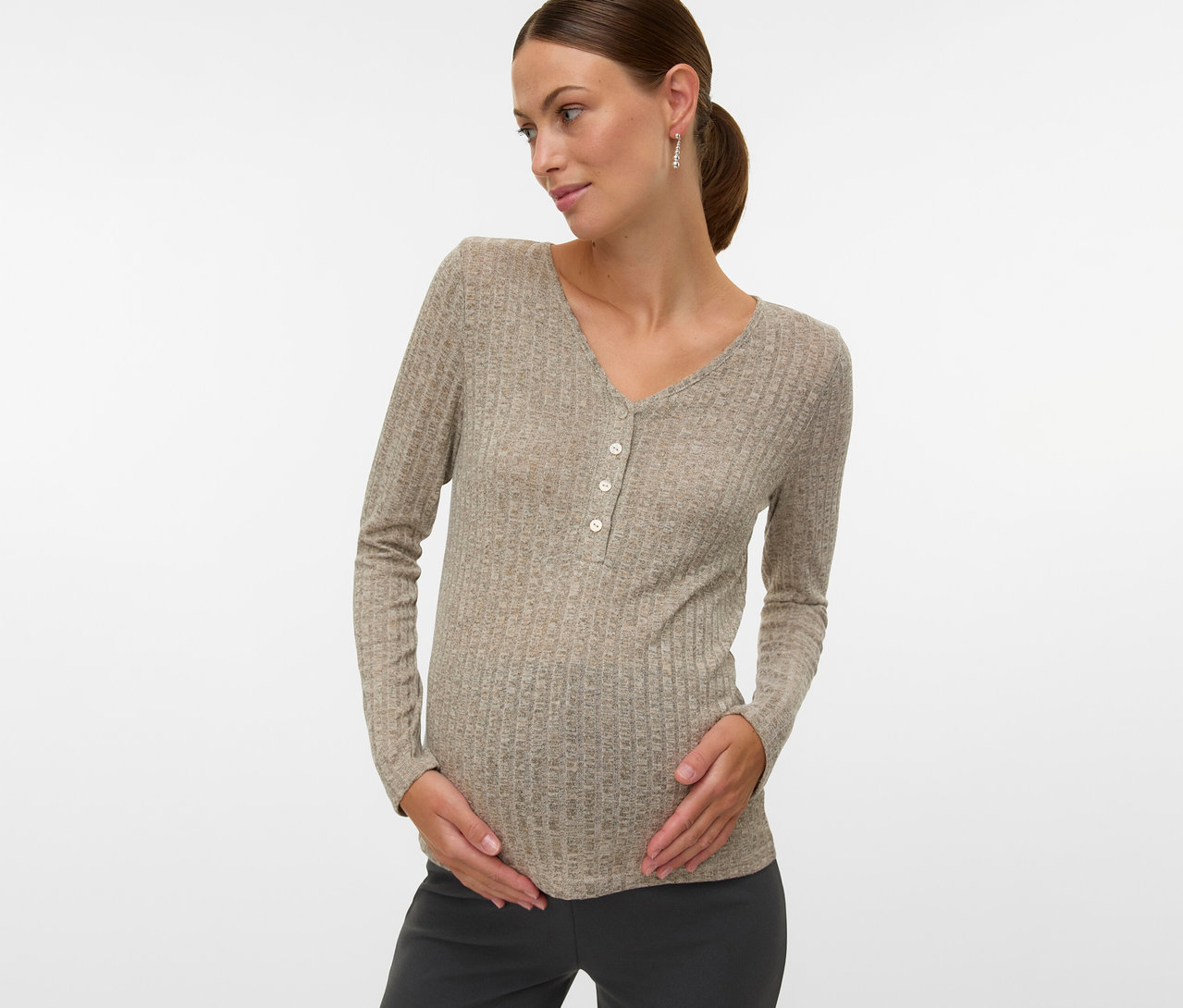 Kobieta w ciąży w koszulce MAMALICIOUS „MLPAMMIE LIA” z długimi rękawami i guzikami, trzymająca się za brzuch.