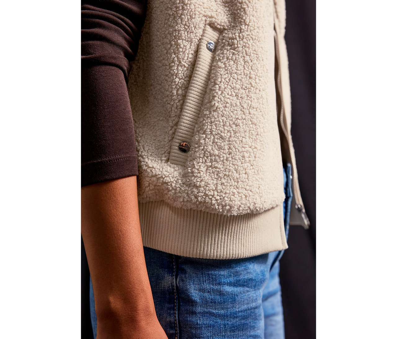 Zbliżenie na osobę ubraną w pluszową kamizelkę Street One i dżinsy.