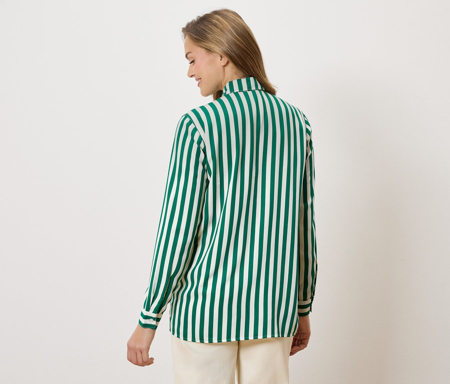 Kobieta od tyłu w bluzce w zielono-białe paski i beżowych spodniach.