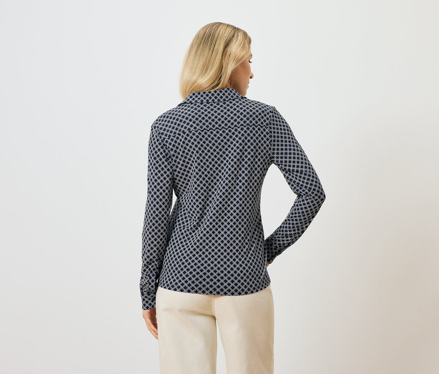 Widok z tyłu blondynki w bluzce z długim rękawem w niebieski wzór i jasnych spodniach.